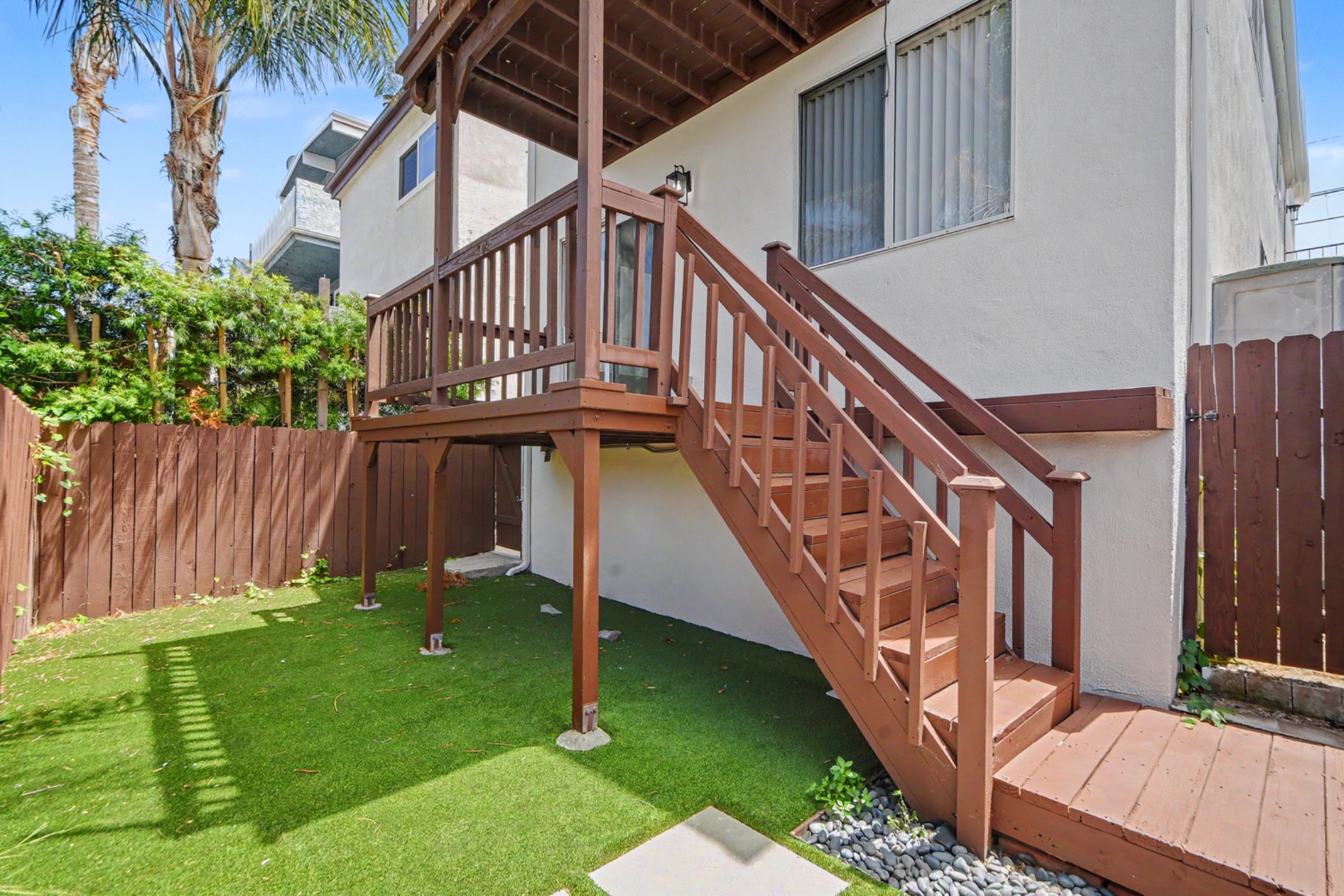 Private backyard with wood deck, exterior stairs, and artificial turf